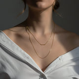 Close-up of a person wearing a delicate gold necklace against a neutral background