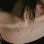 Close-up of a person wearing a gold necklace with a blurred background