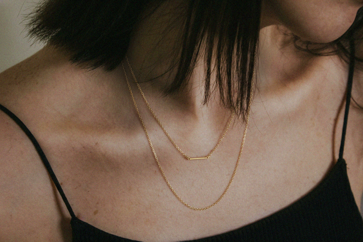 Close-up of a person wearing a gold necklace with a blurred background