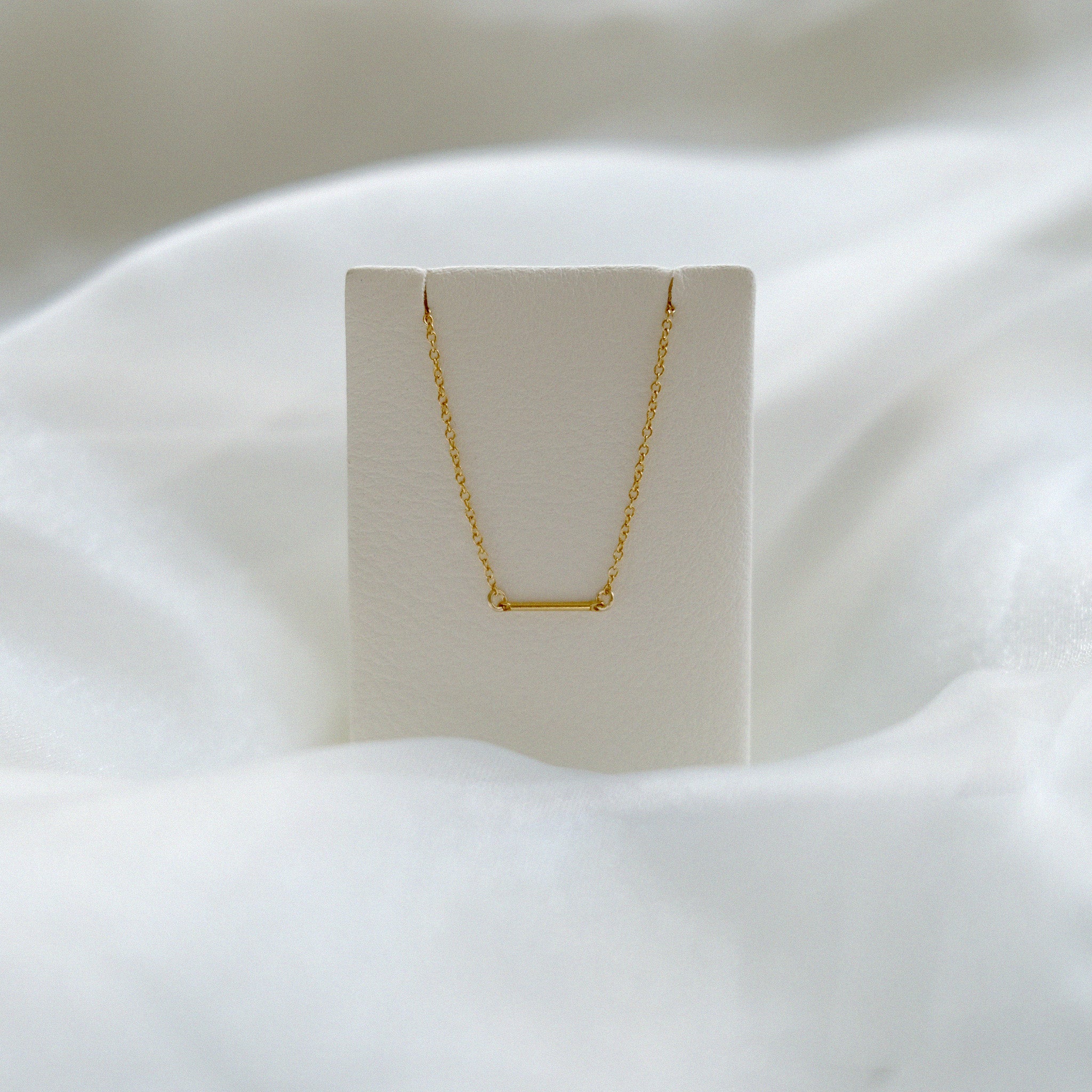 Gold necklace on a white stand with a soft white background
