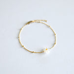 Gold bracelet with a small mother of pearl daisy flower charm on a light gray background