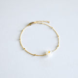 Gold bracelet with a small mother of pearl daisy flower charm on a light gray background