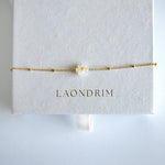 Gold bracelet with a flower charm on a white card displaying 'LAONDRIM'.