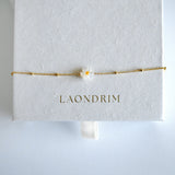 Gold bracelet with a flower charm on a white card displaying 'LAONDRIM'.