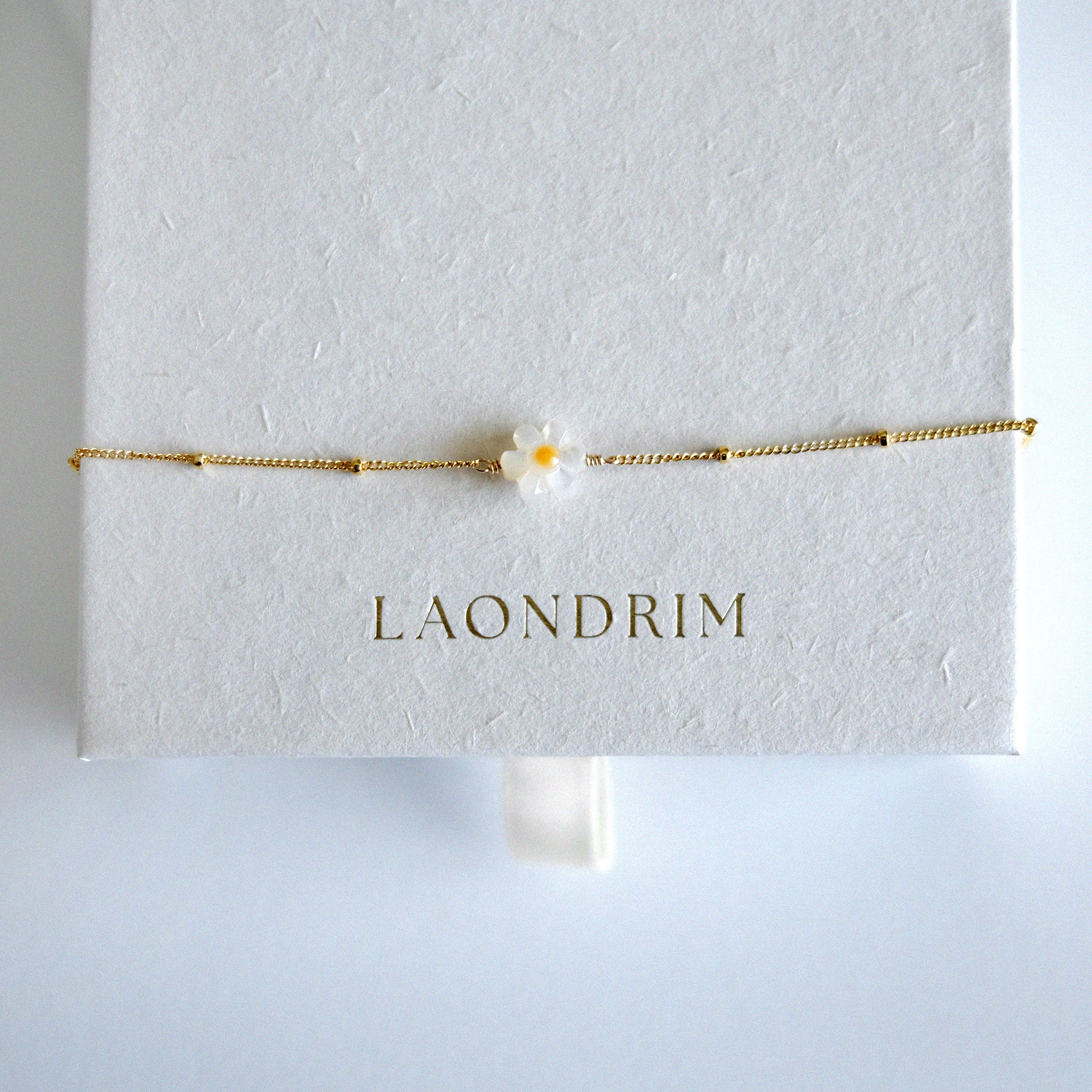 Gold bracelet with a flower charm on a white card displaying 'LAONDRIM'.