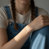 Person wearing a delicate bracelet with a daisy flower charm, sitting on a surface.