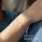Gold Chain with mother of pearl daisy charm bracelet on a wrist.