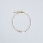 Gold bracelet with a single pearl on a light gray background