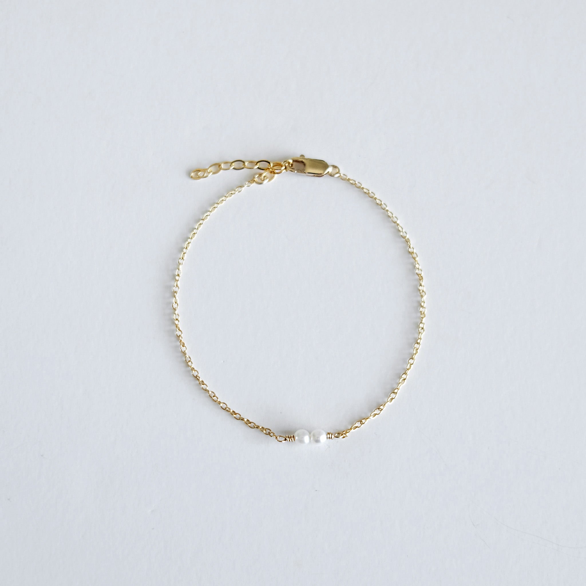 Gold bracelet with a single pearl on a light gray background