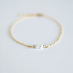 Gold bracelet with a single pearl on a light gray background