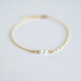 Gold bracelet with a single pearl on a light gray background