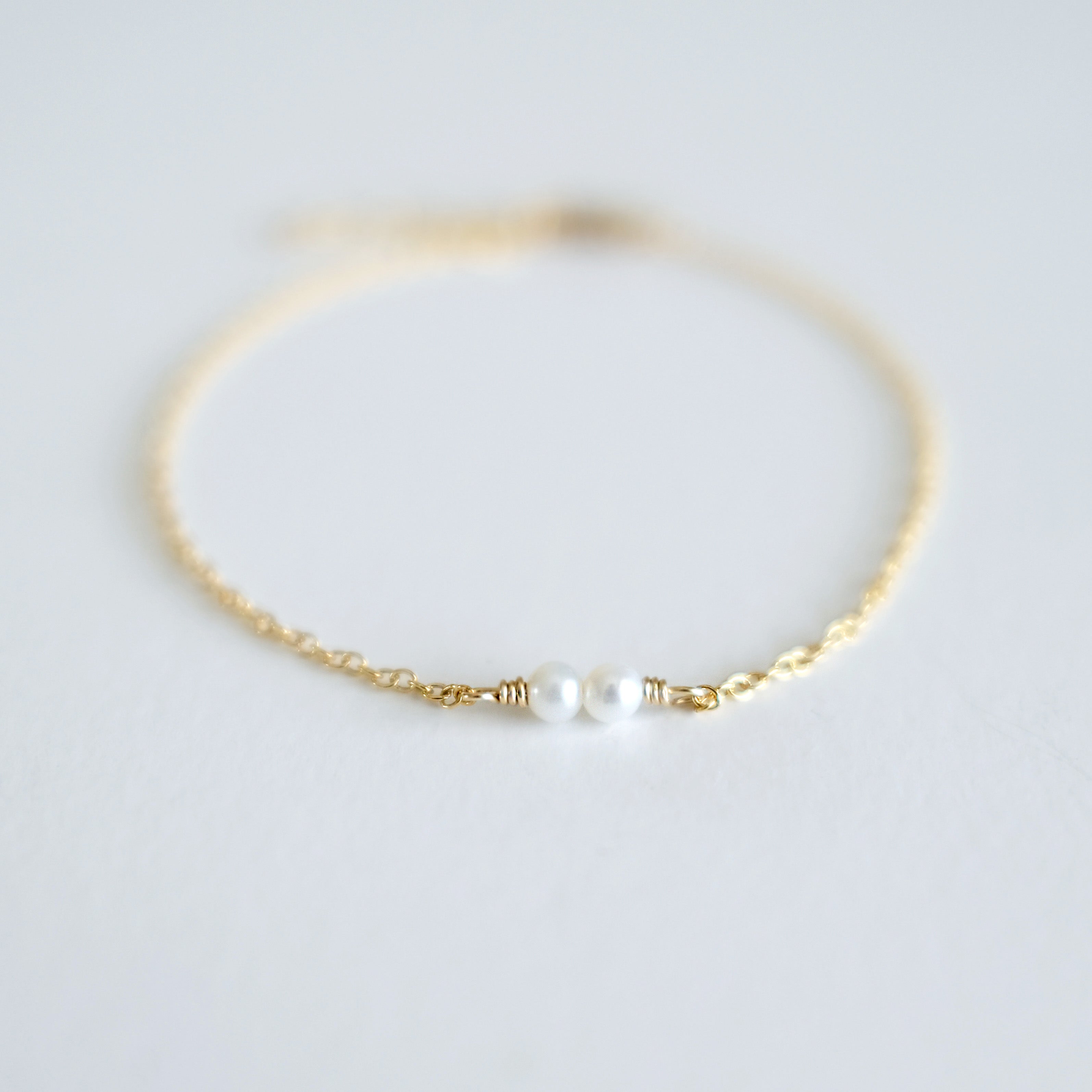 Gold bracelet with a single pearl on a light gray background
