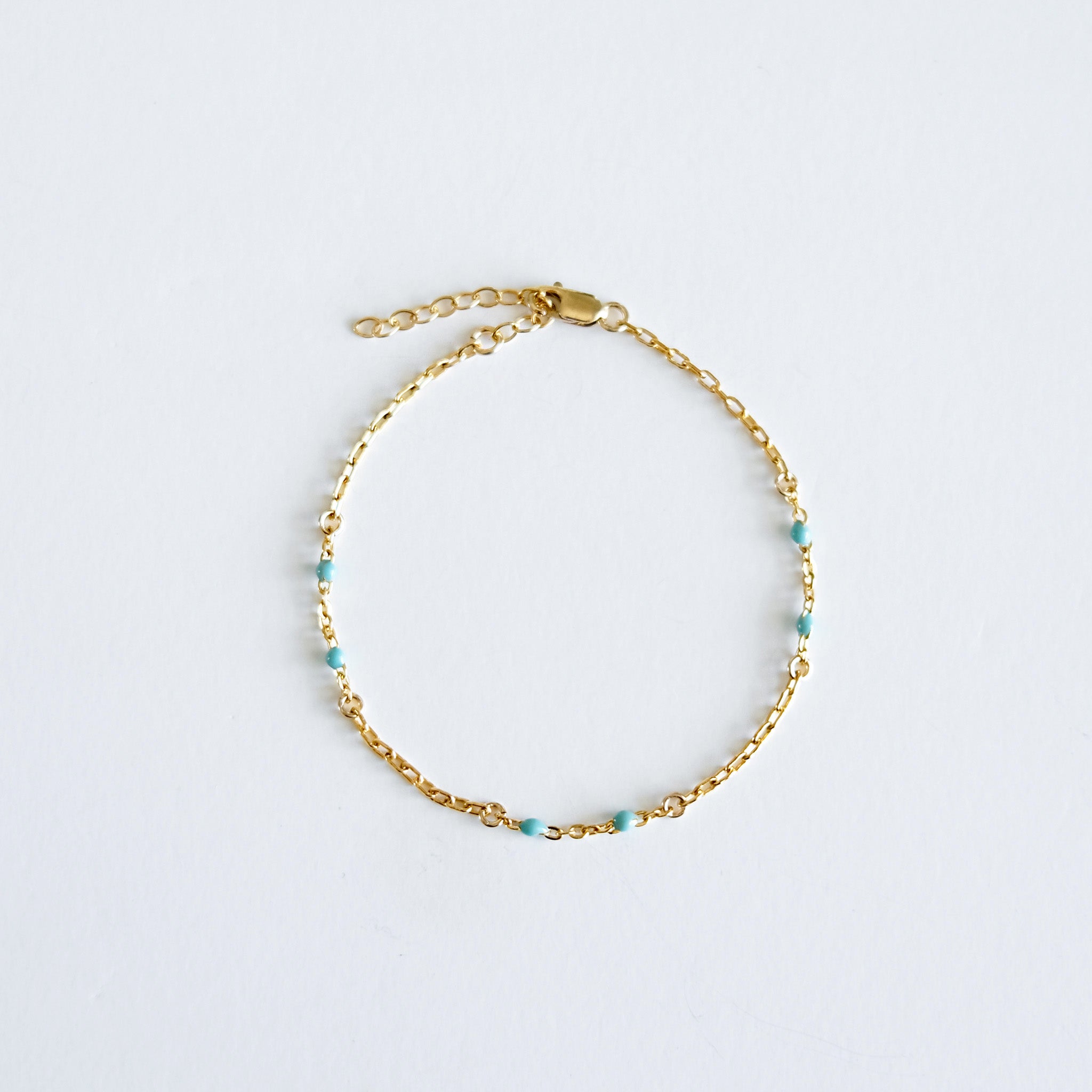 Gold bracelet with mint colour enamel accent on a light gray background