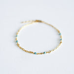 Gold bracelet with small beads on a light gray background