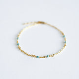Gold bracelet with small beads on a light gray background