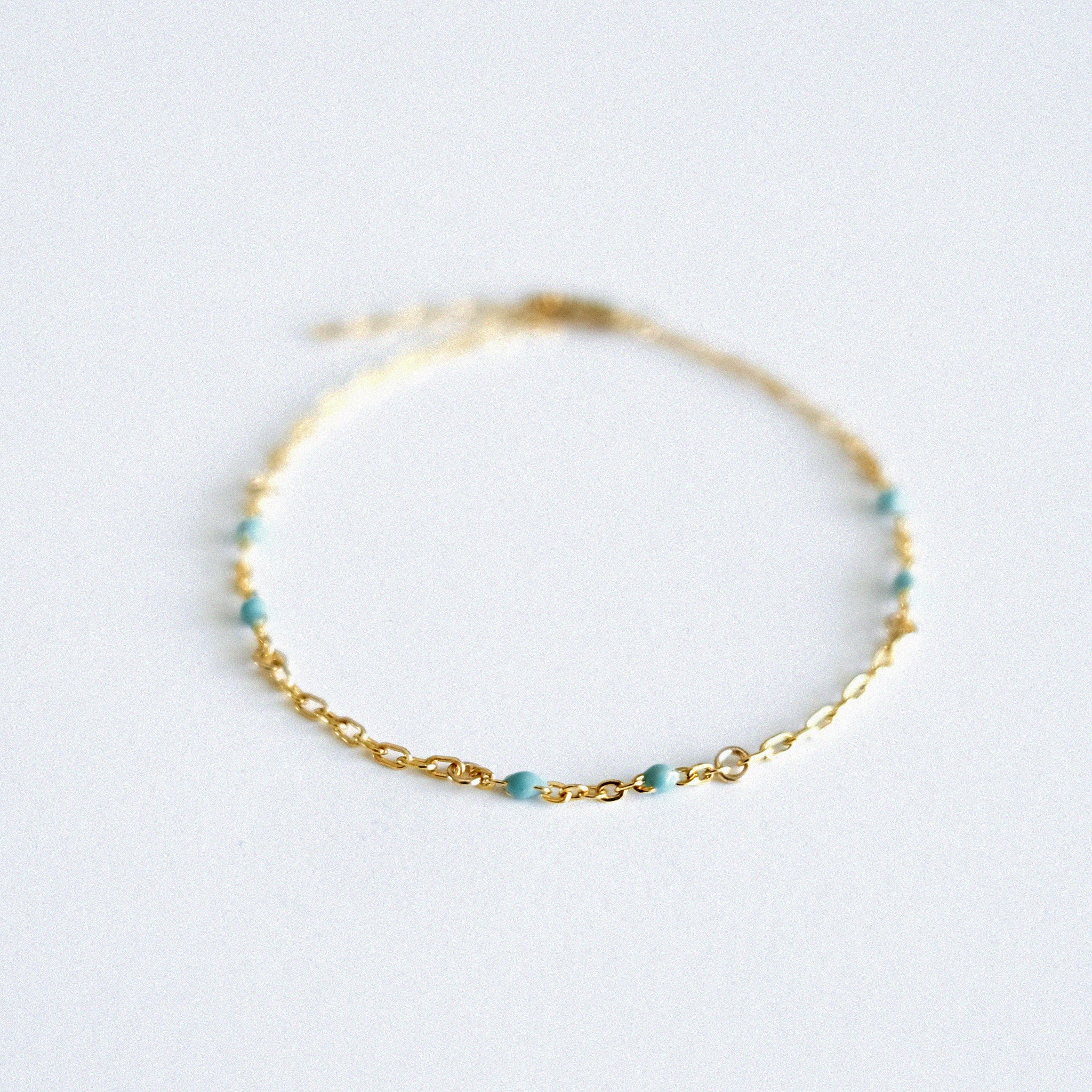 Gold bracelet with small beads on a light gray background