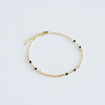 Gold bracelet with black beads on a light gray background
