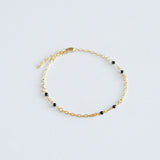 Gold bracelet with black beads on a light gray background