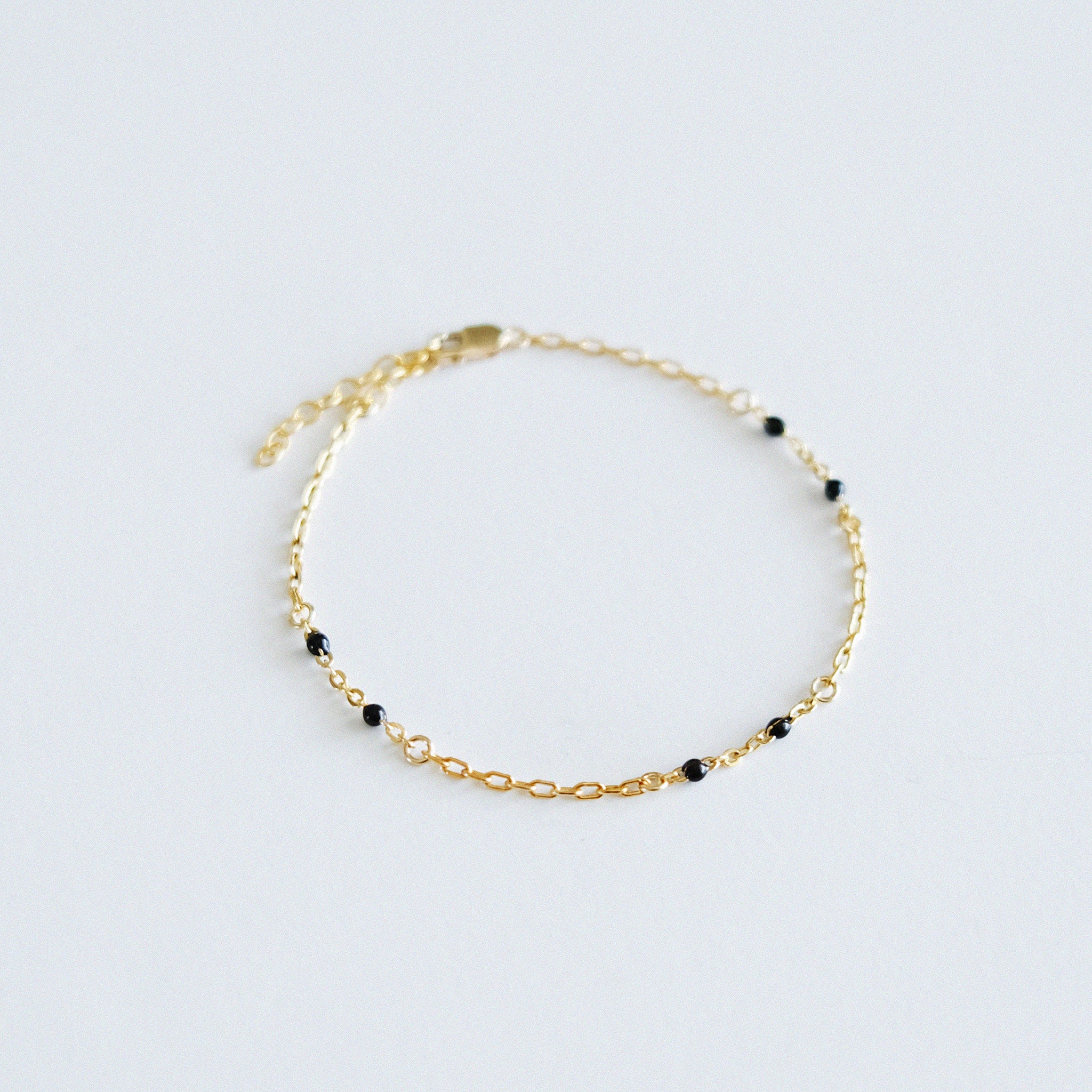 Gold bracelet with black beads on a light gray background