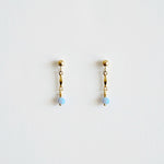 Pair of gold earrings with blue beads on a light gray background