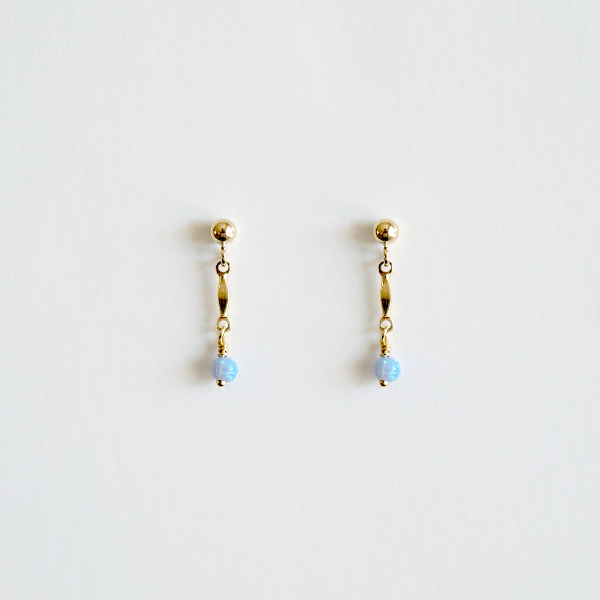 Pair of gold earrings with blue beads on a light gray background
