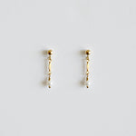 Pair of gold earrings with pearl drops on a light gray background