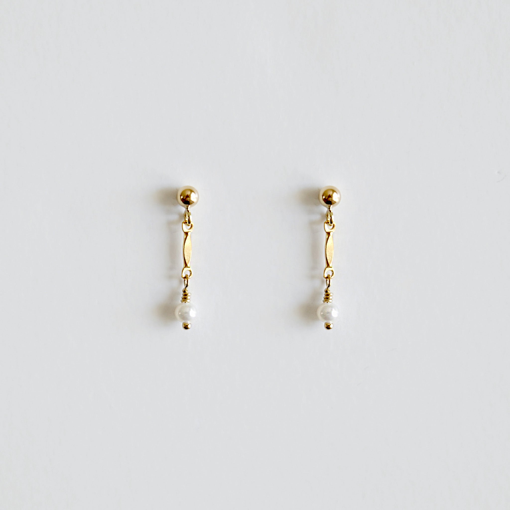 Pair of gold earrings with pearl drops on a light gray background