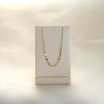 Gold necklace on a white necklace stand against a beige background