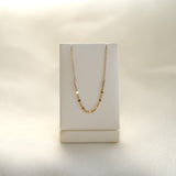 Gold necklace on a white necklace stand against a beige background