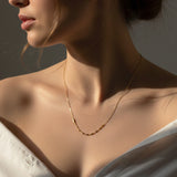 Close-up of a woman wearing a delicate gold necklace against a neutral background