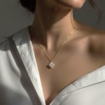 Gold necklace with a clover pendant worn by a person in a white shirt.