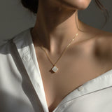 Gold necklace with a clover pendant worn by a person in a white shirt.