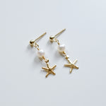 Pair of earrings with starfish and pearl designs on a light gray background