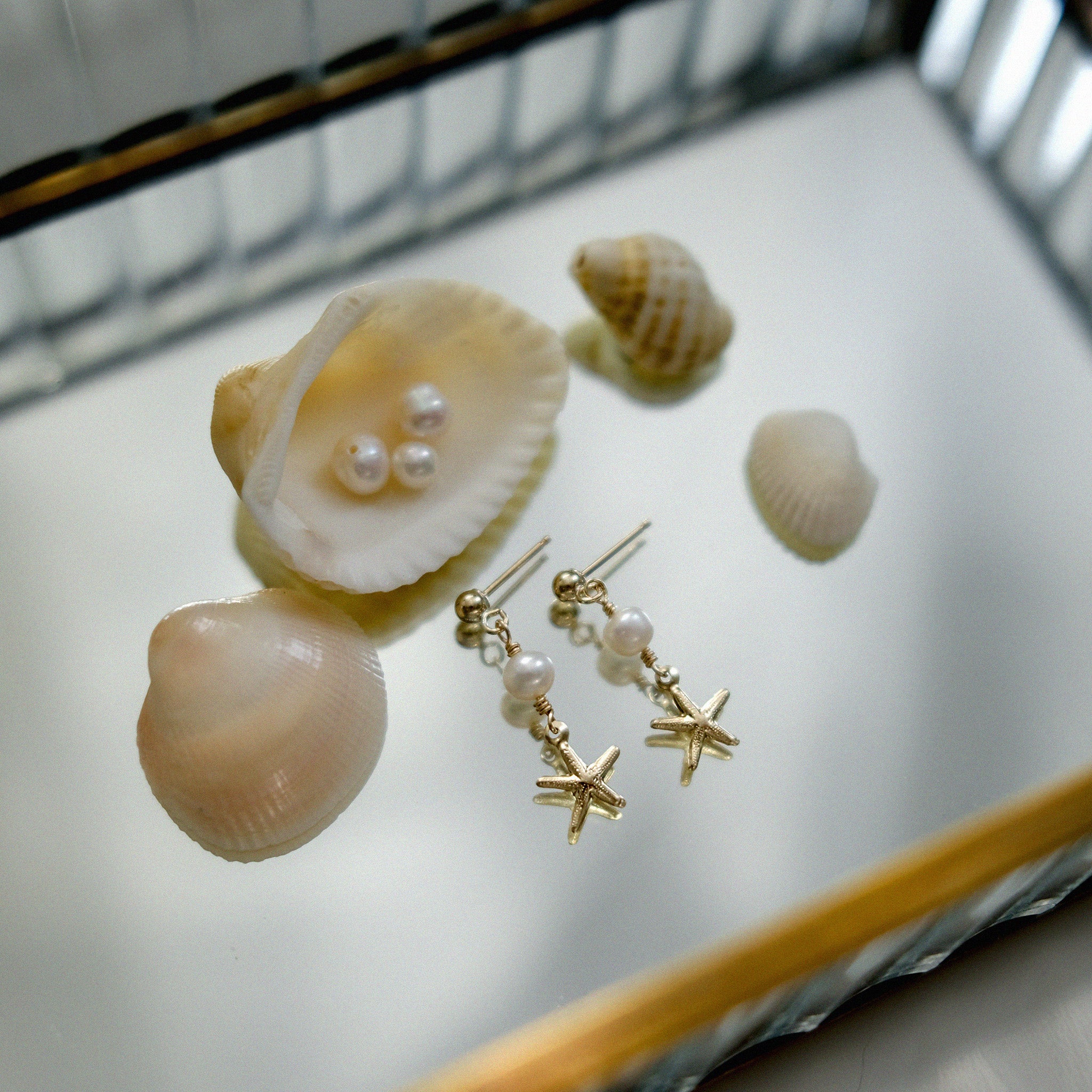 Pearl and Starfish pendant gold earrings displayed on the reflexed jewellery box with shells and pearls.