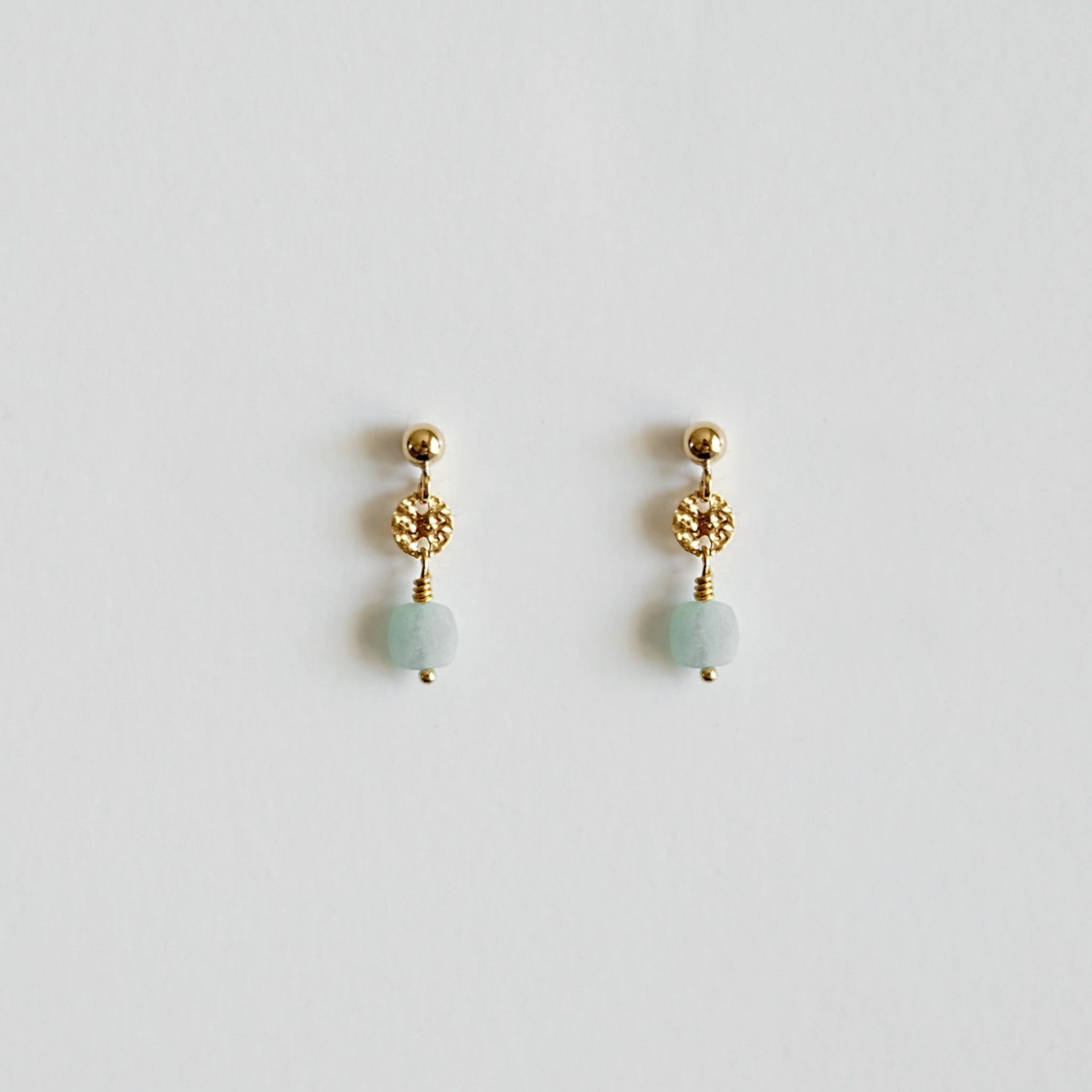 Pair of gold earrings with green beads on a light gray background