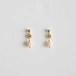 Pair of gold earrings with pink beads on a light gray background