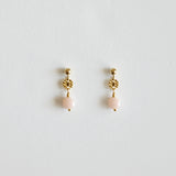Pair of gold earrings with pink beads on a light gray background