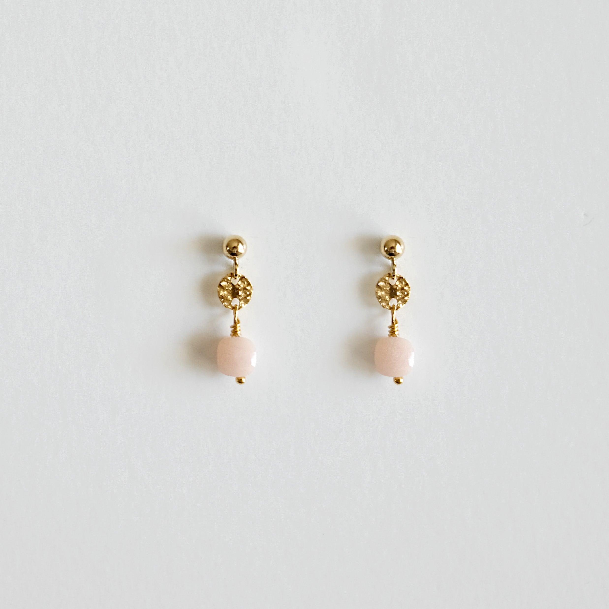 Pair of gold earrings with pink beads on a light gray background