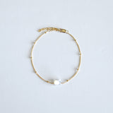 Gold bracelet with a single cat shaped pearl on a light gray background