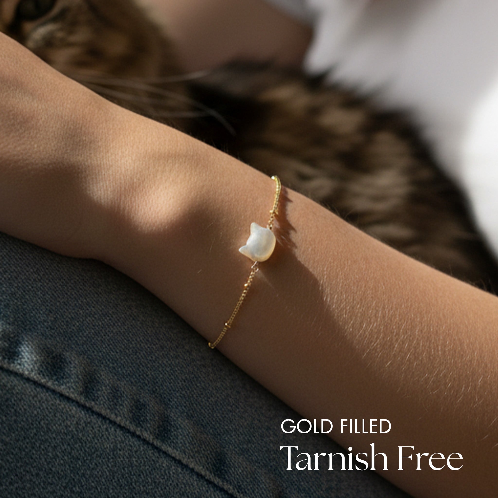 Gold filled bracelet with a cat shaped pearl on a wrist, cat in the background