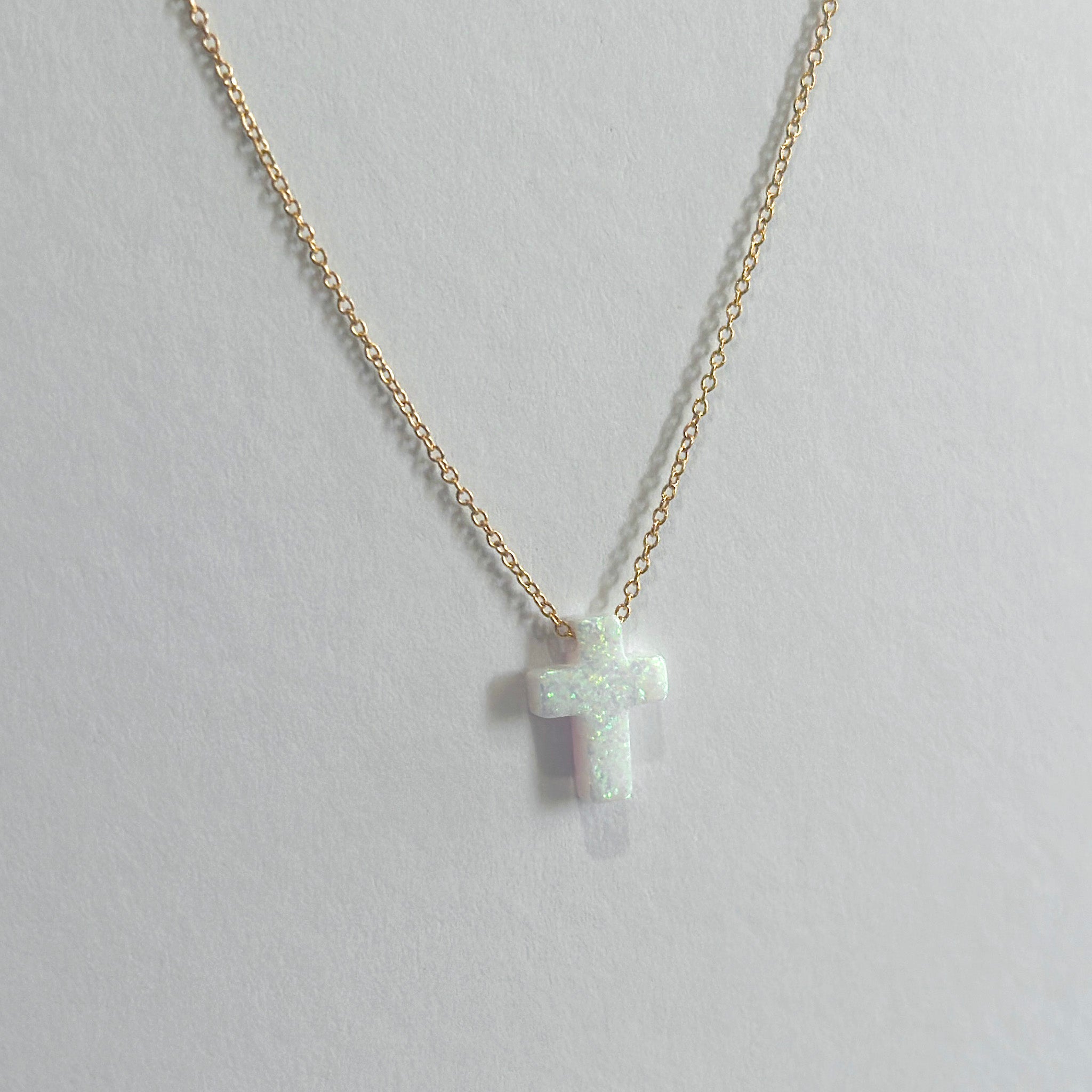 Gold necklace with a small cross pendant on a light gray background