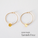 Gold-filled Aster hoop earrings with 5mm disc accent laid flat on a white background