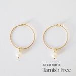 Gold-filled hoop earrings with freshwater pearl accent laid flat on white surface