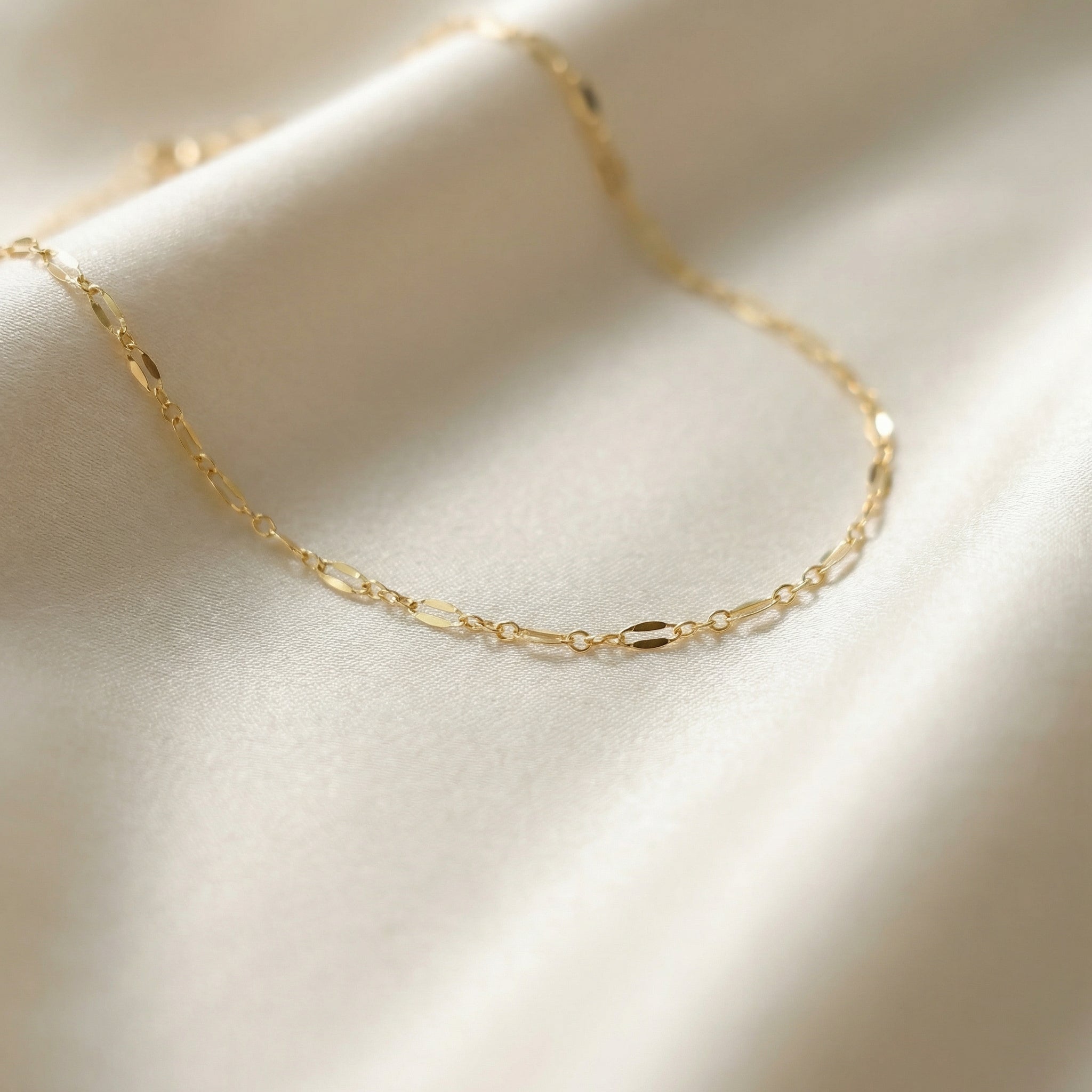 Gold chain necklace on a soft beige fabric background