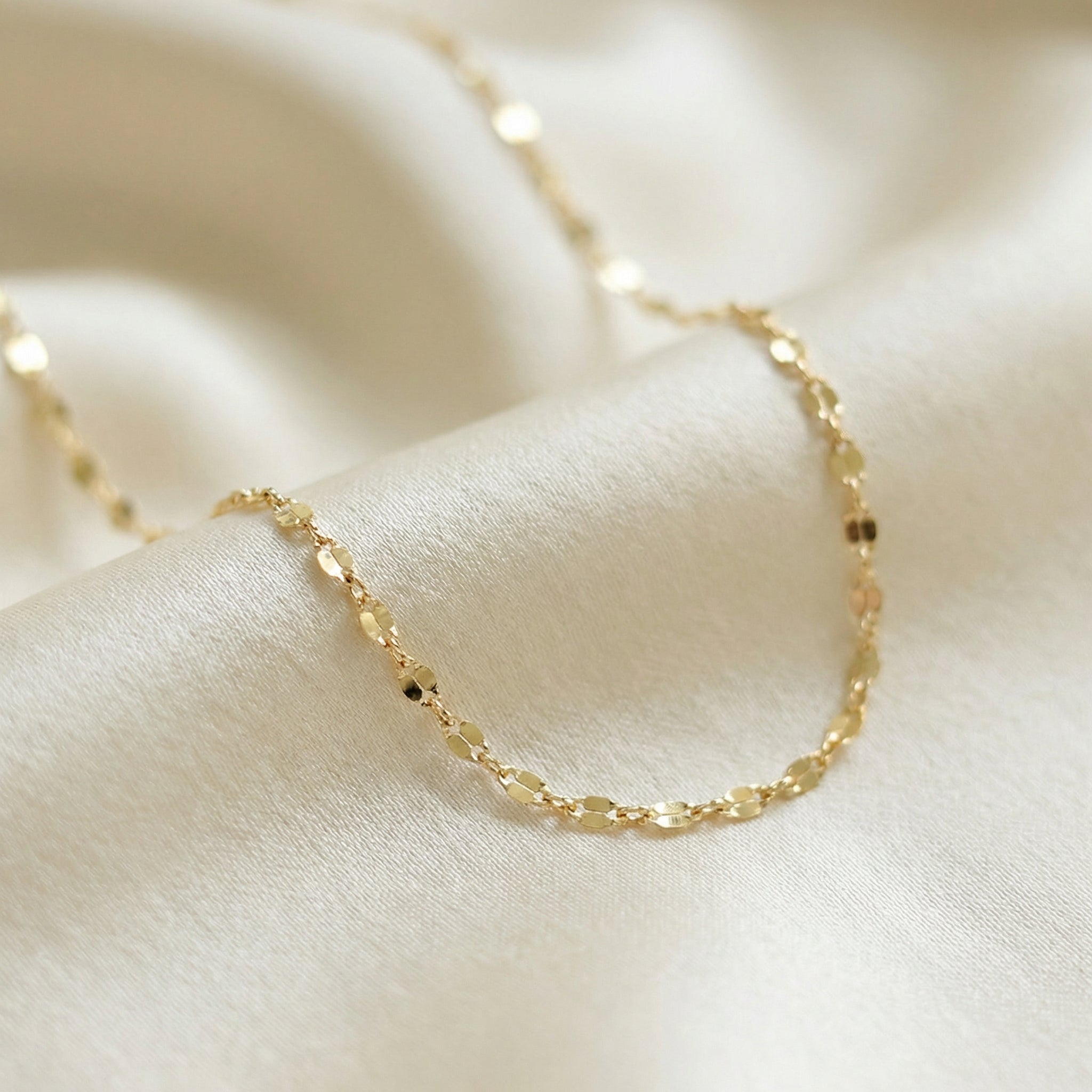 Gold chain necklace on a soft beige fabric background
