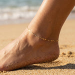 Ankle with gold anklet on sandy beach