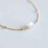 Gold bracelet with a cat face shaped mother of pearl on a light gray background