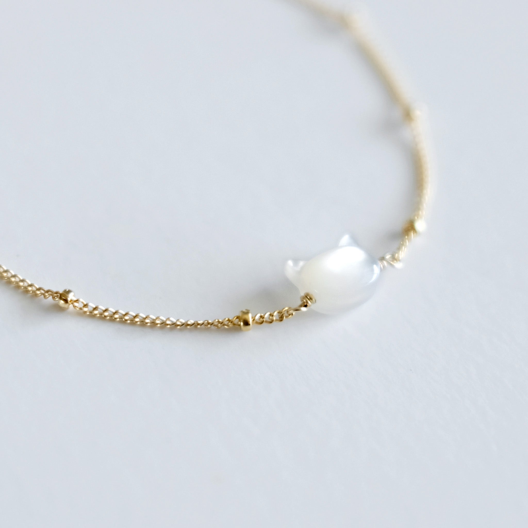 Gold bracelet with a cat face shaped mother of pearl on a light gray background