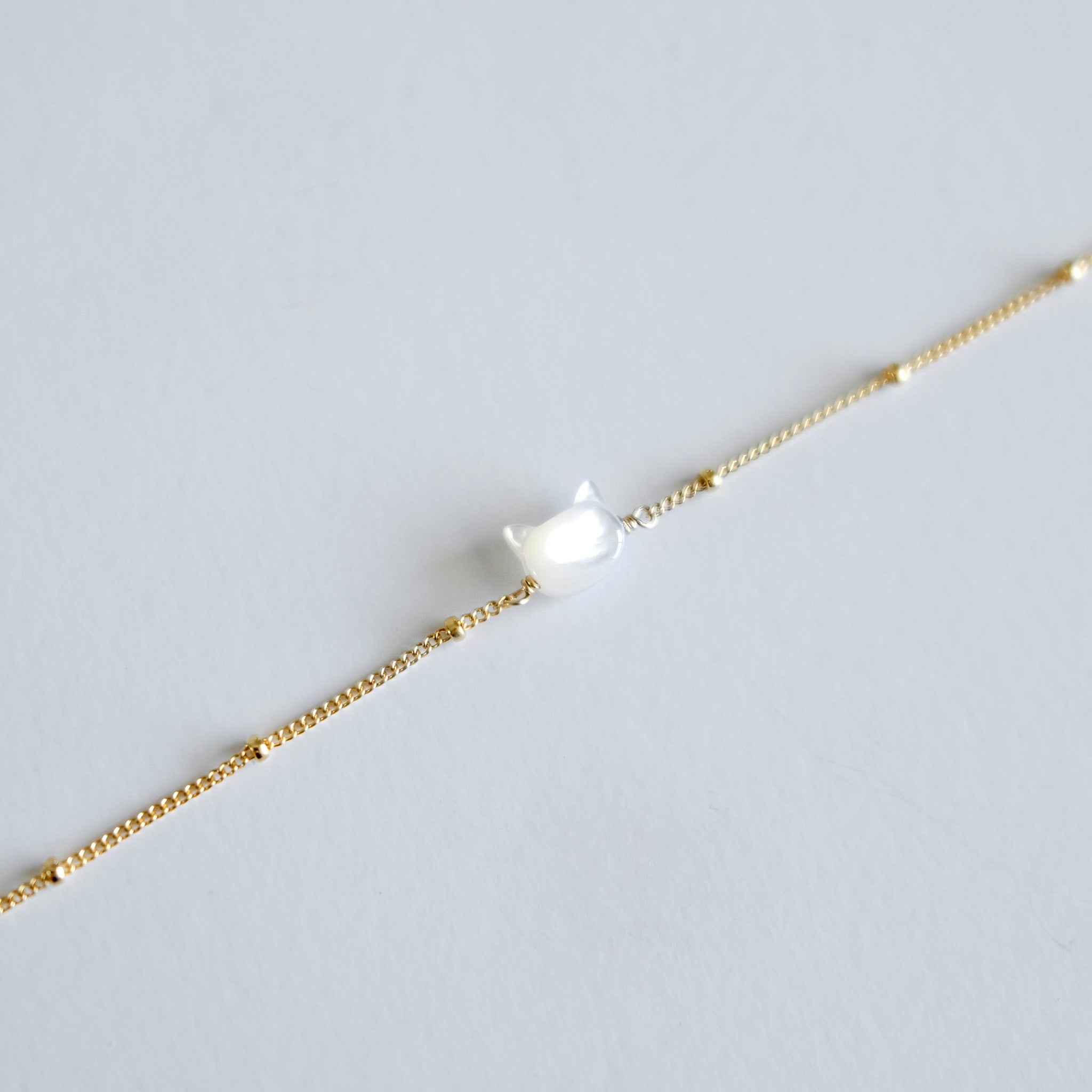 Gold bracelet with a small cat face shaped charm on a light gray background