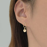 Model wearing Celina Disc Earrings solo, reflecting light on earlobe